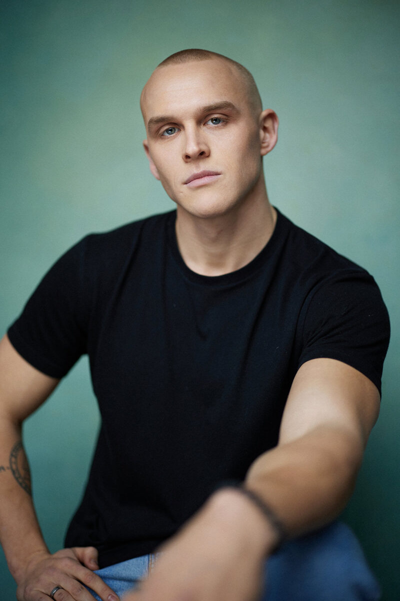 Montreal-actors-headshot-black-t-shirt-tattoo-bracelet-shaved-head-turquoise-canvas-background-by-nadia-zheng