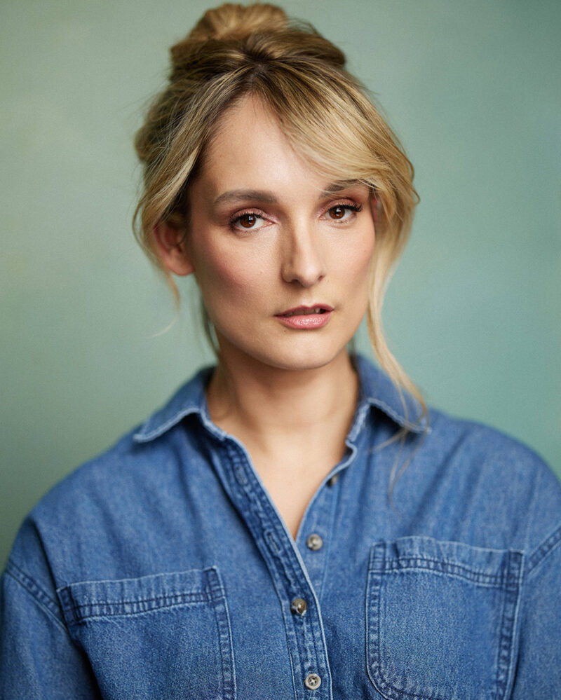 Montreal-actress-headshot-tied-up-hair-jeans-top-teal-background