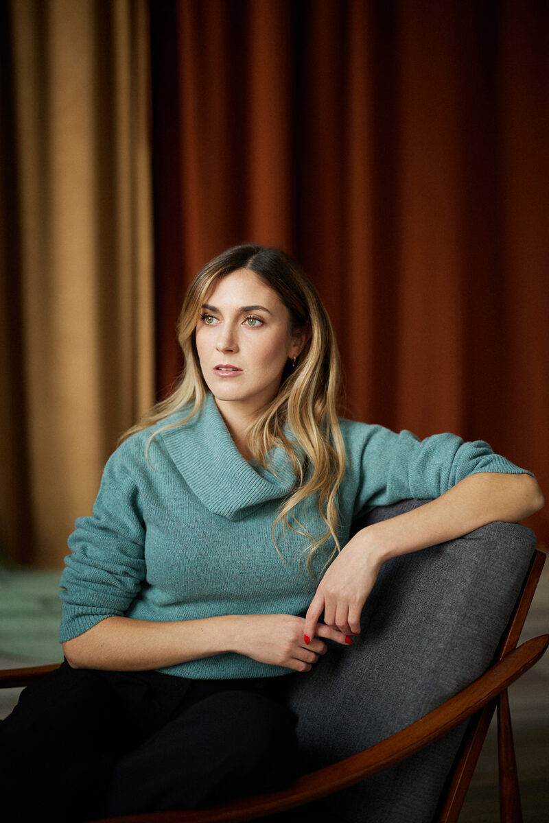 Montreal-actress-headshot-torso-blue-sweater-midcentury-chair-red-yellow-curtain-by-nadia-zheng