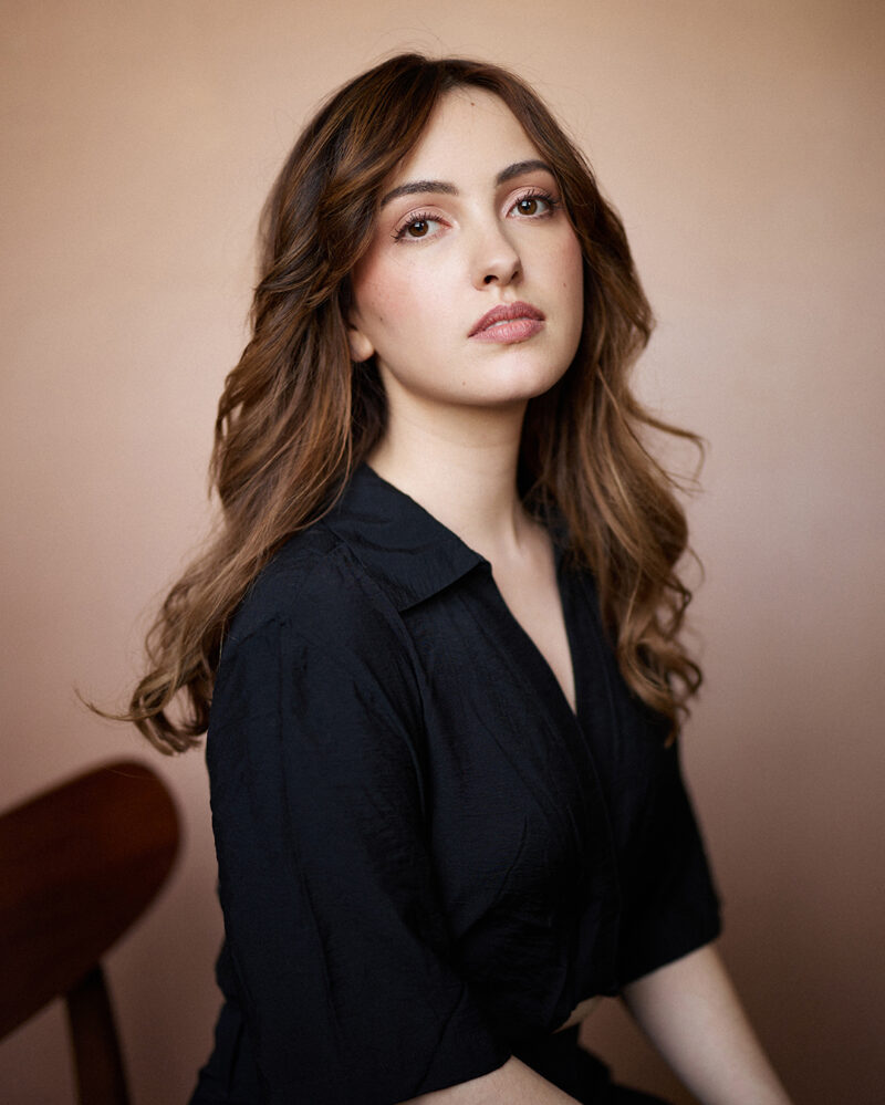 Montreal-actress-headshot-casting-black-top-beige-background-wooden-chair-by-nadia-zheng